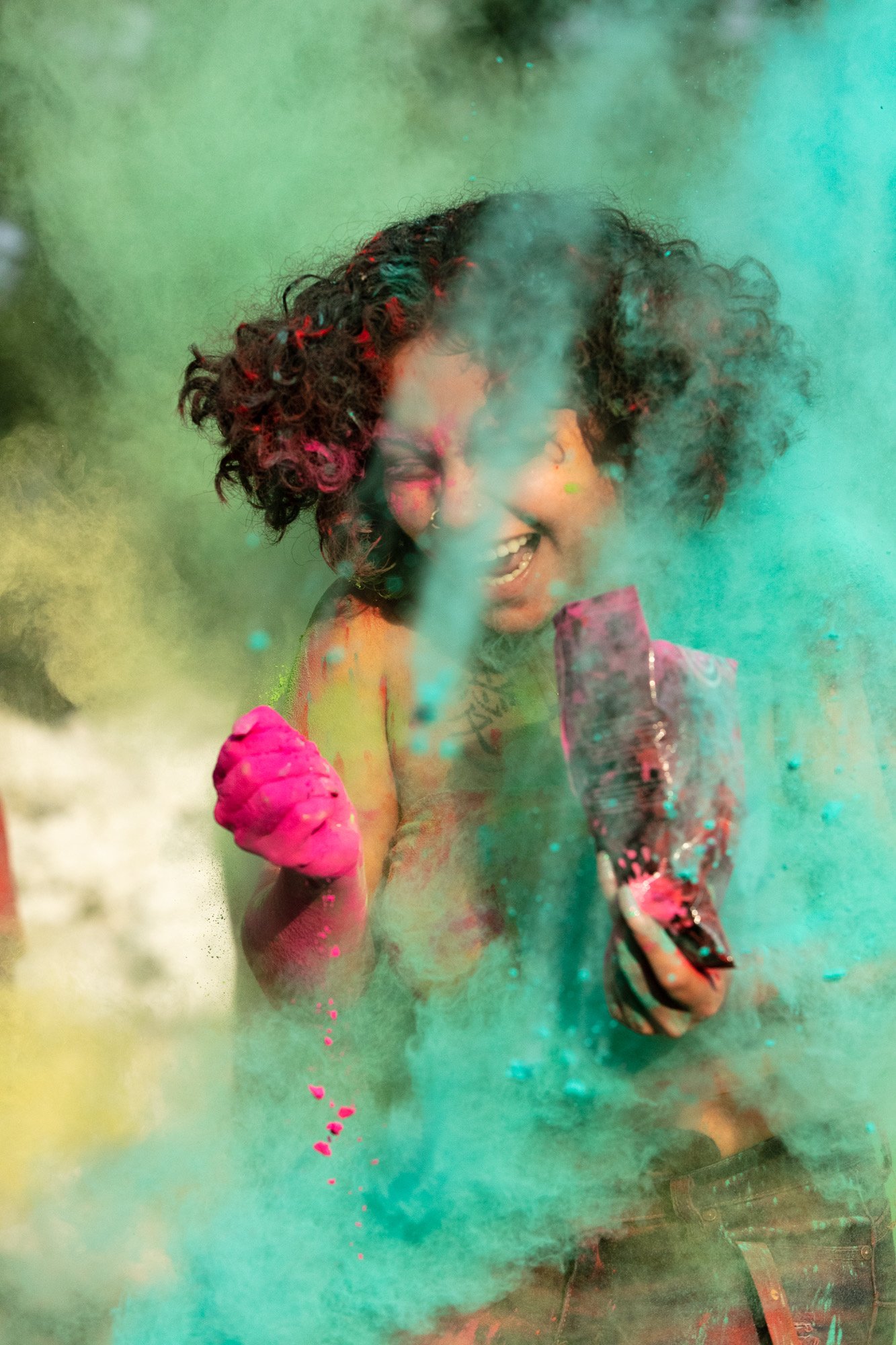 female student with curly hair smiles broadly as she's covered with blue powder paint. 