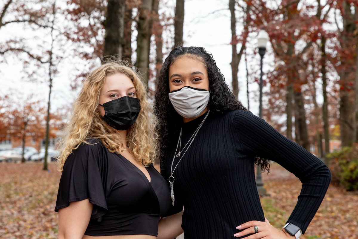 Two female students stand together while wearing masks. 