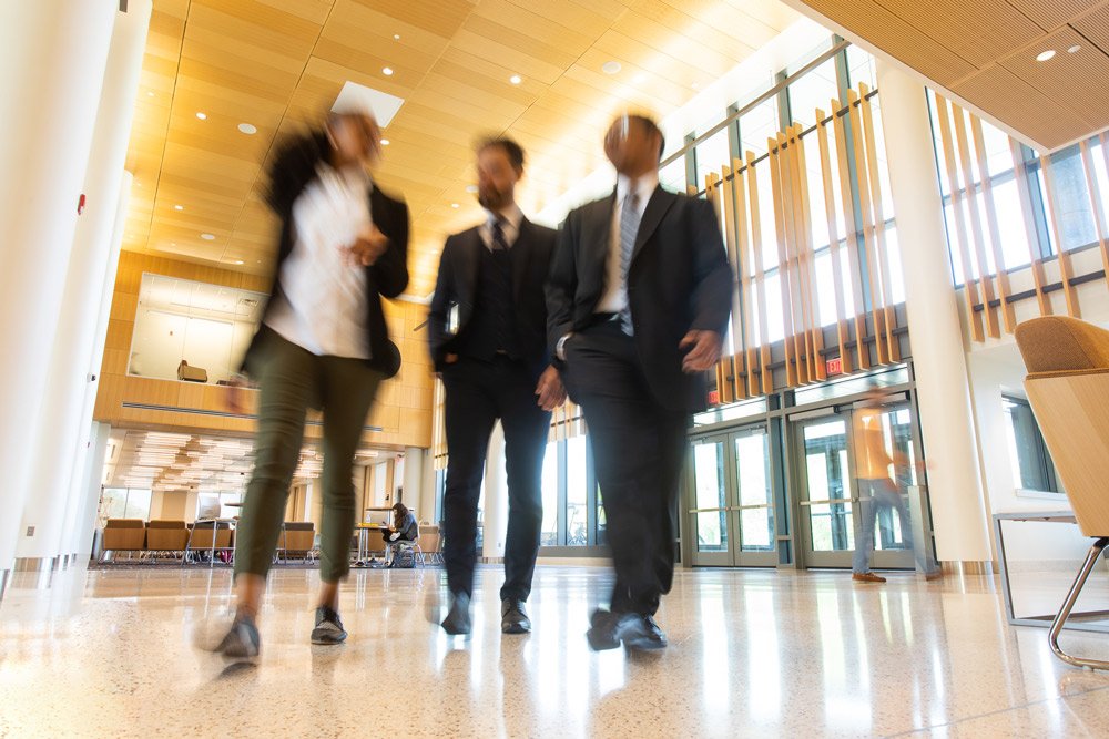Rowan University students walk through Business Hall, with a blur effect on their moving bodies.