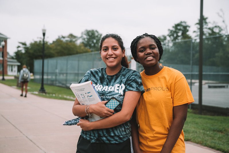 Two students smiling by the tennis courts.
