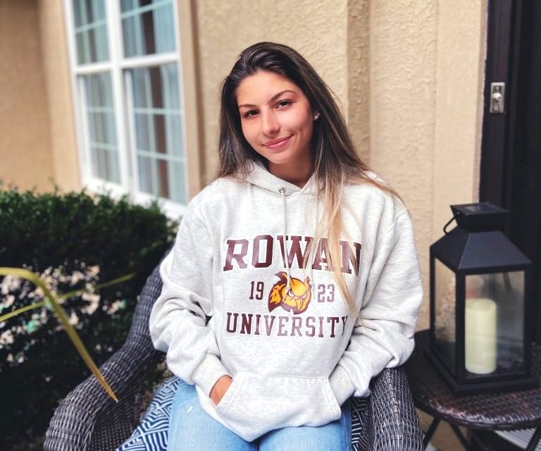 Julia sits in a chair at home, while wearing a Rowan sweatshirt. 