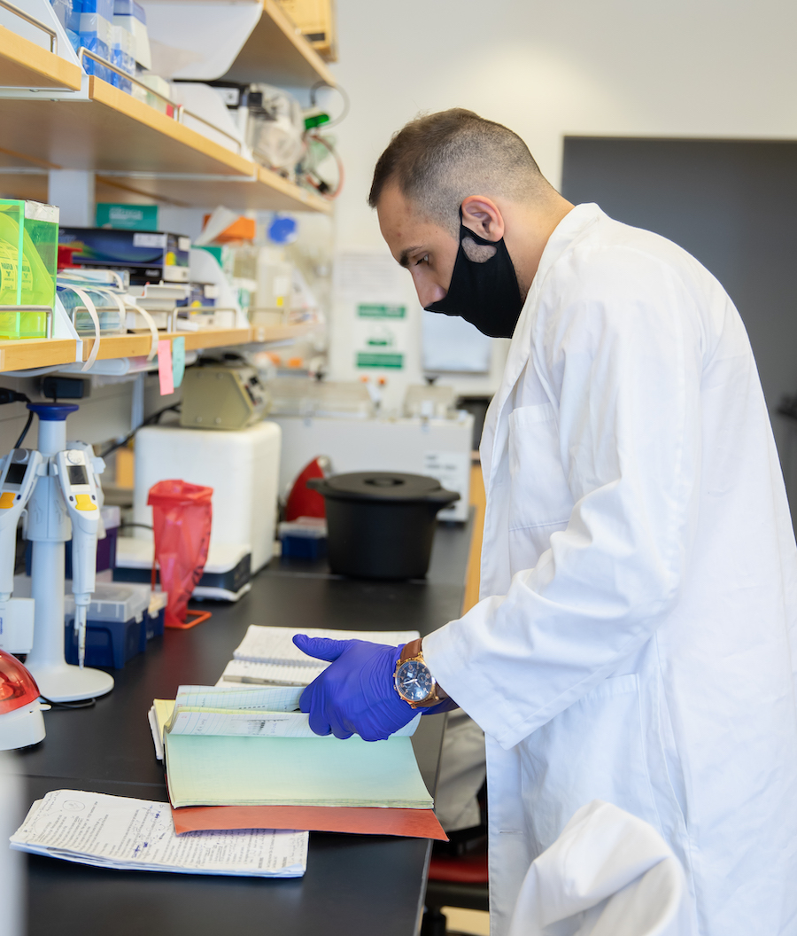 Side view of student working in lab, wearing lab coat and mask.