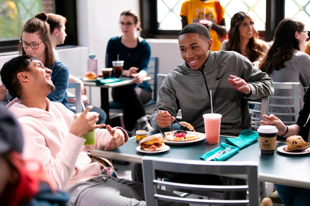 Rowan University students smile and laugh while eating their meal on campus.