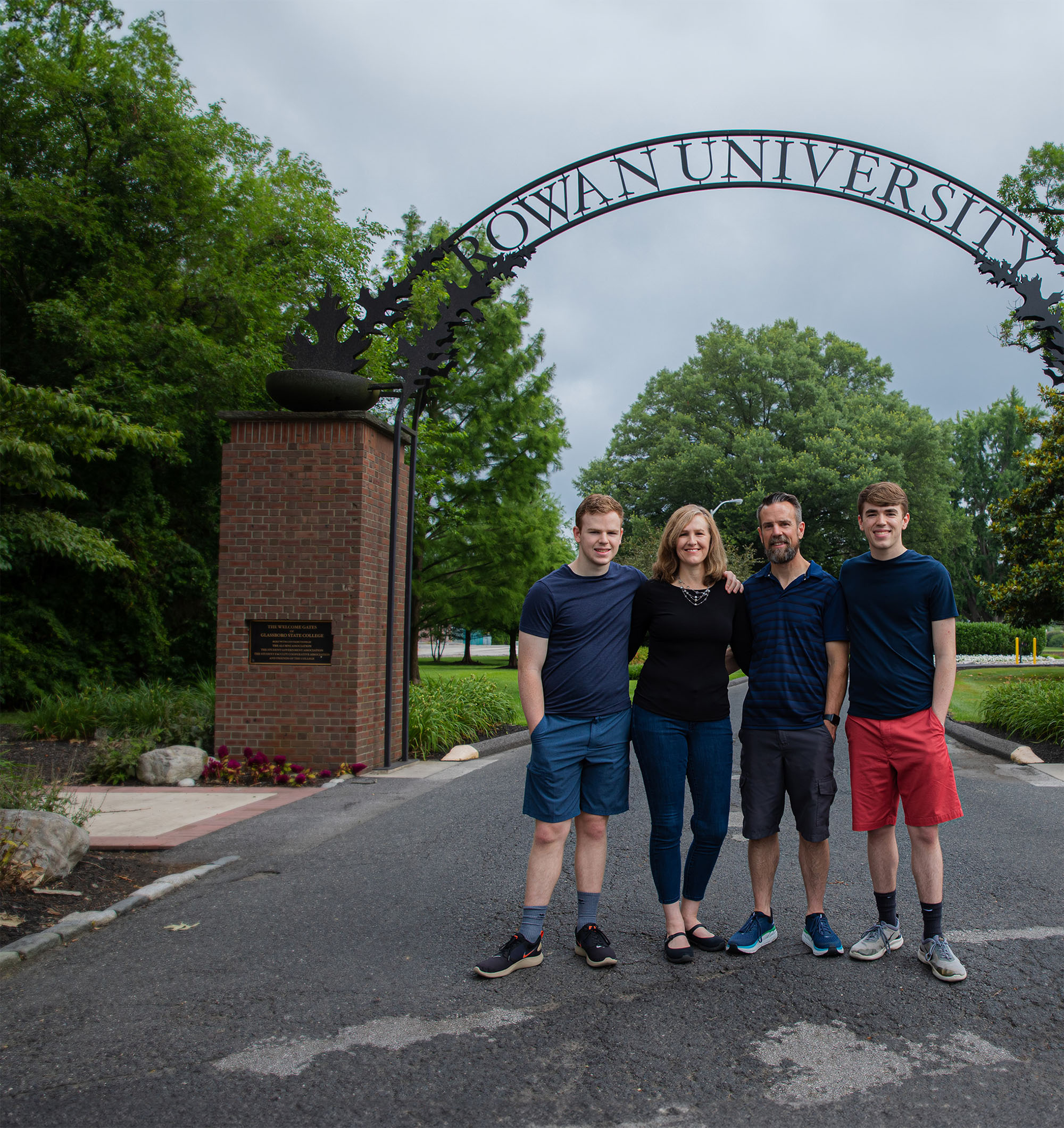 A family of four poses for a photo under the Rowan University arch.