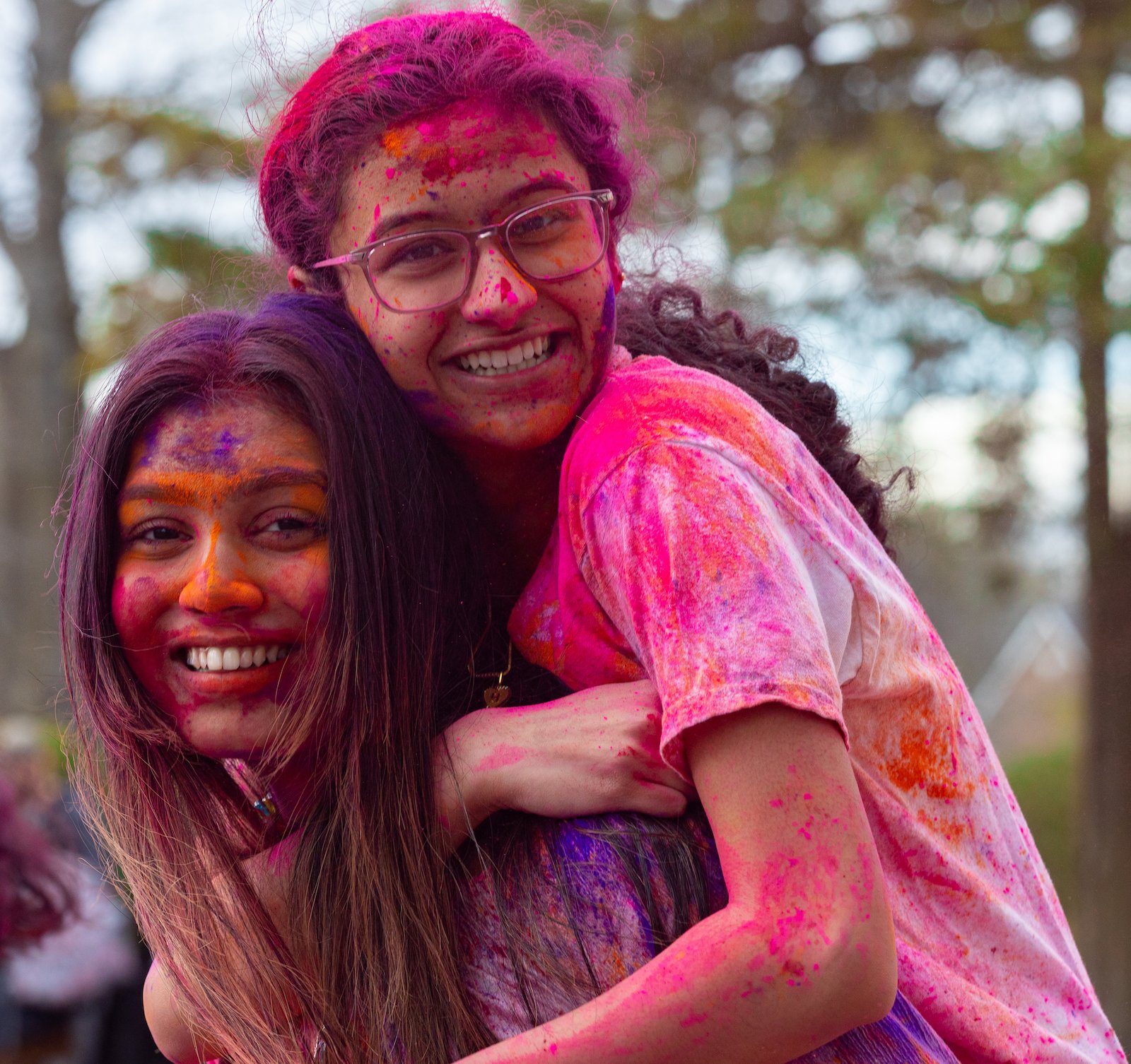 Two Rowan University female students jump together during Holi, with faces and bodies filled with paint.