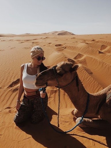 A girl sitting next to a camel.