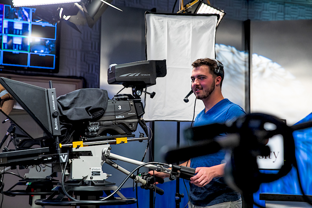 A Rowan University student smiles with a video camera while working.