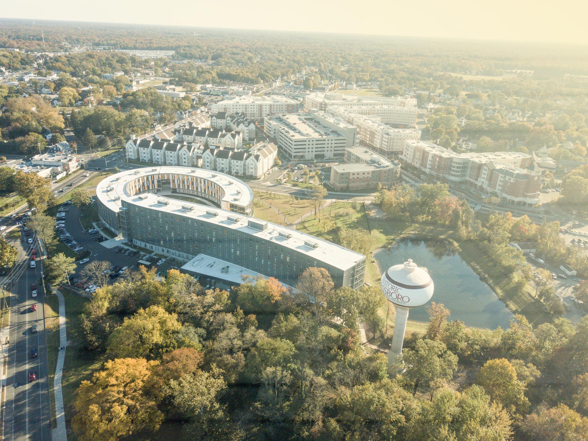 hazy drone image of rounded residence hall Holly Pointe Commons, with trees and town of Glassboro in the background. 