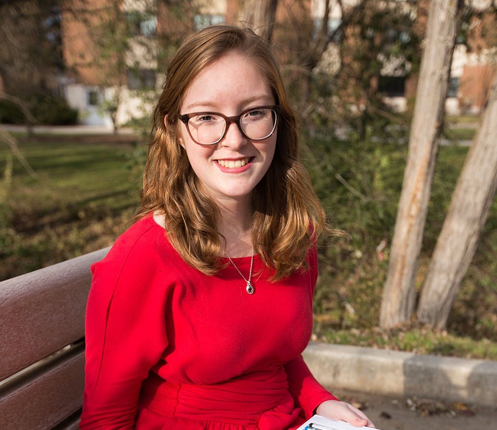 Picture of Melissa on a bench outside of a building on campus