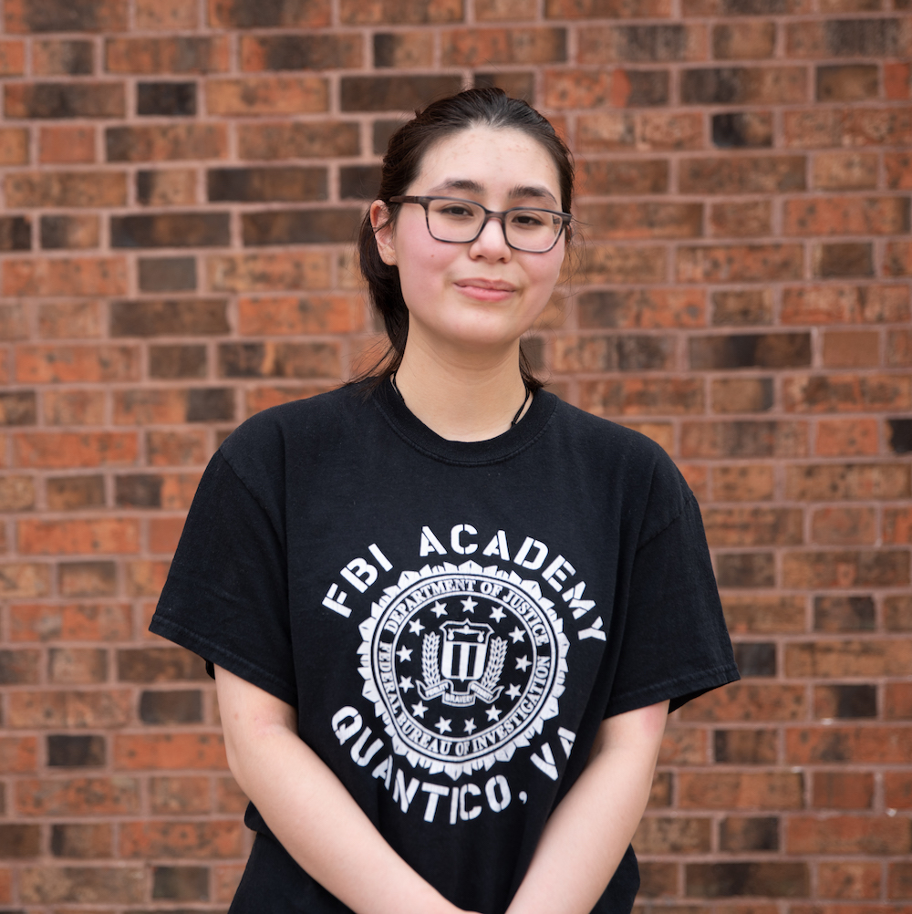 Sofia stands against a brick wall on campus.