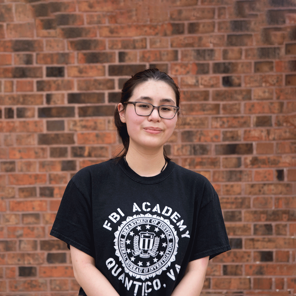 Sofia stands against a brick wall on campus.