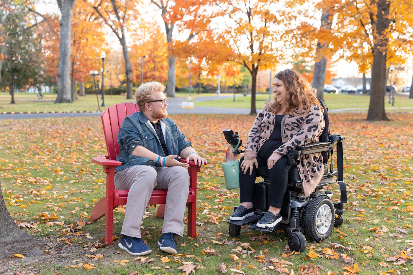 Two Rowan University students smile at each other while socializing, one student in a chair and the other in a wheelchair.
