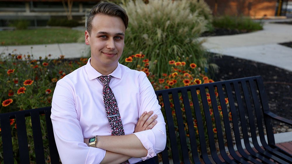Evan wears a shirt and tie in a portrait shot outdoors