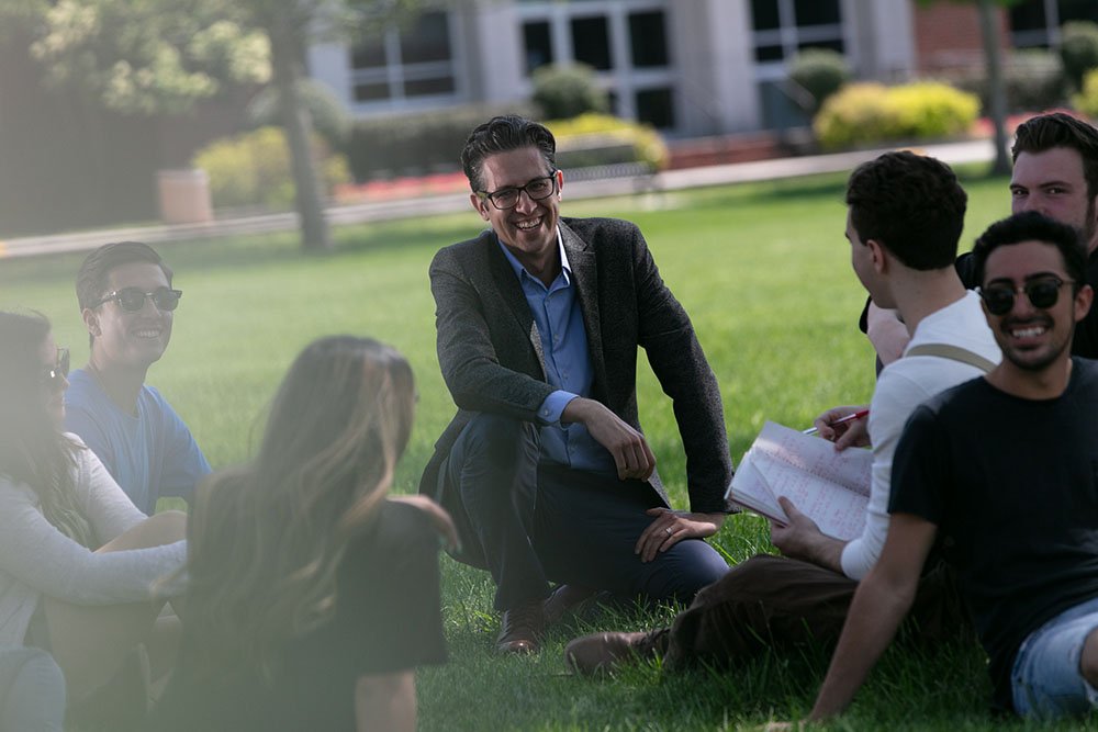 students sitting on lawn with a professor near a tree