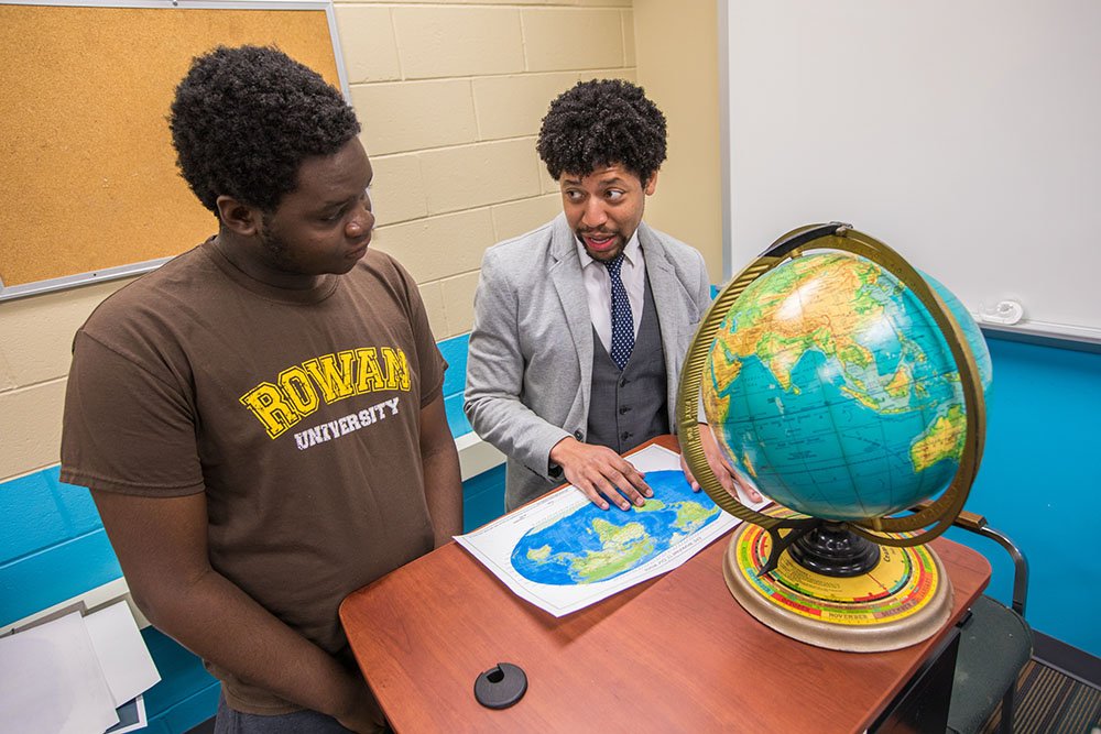 college student sitting with professor looking at a globe