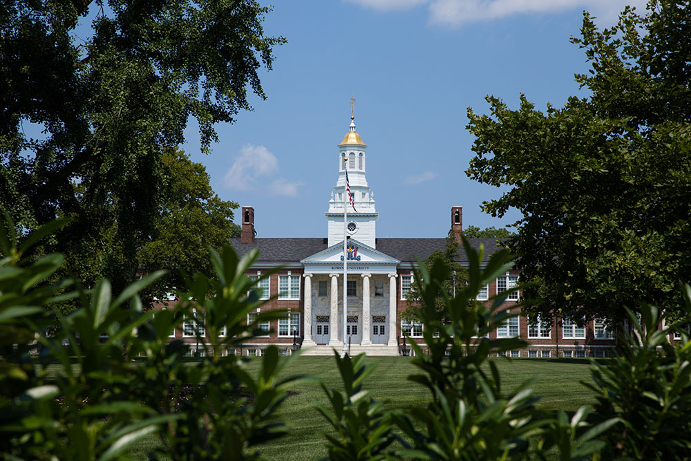 exterior shot of Bunce Hall in summer, shown between bushes. 