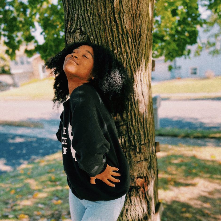 Ariana stands and smiles in front of a shade tree.