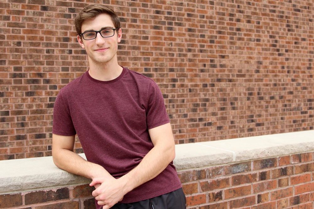 Computer science major Brian C. leaning against a brick wall