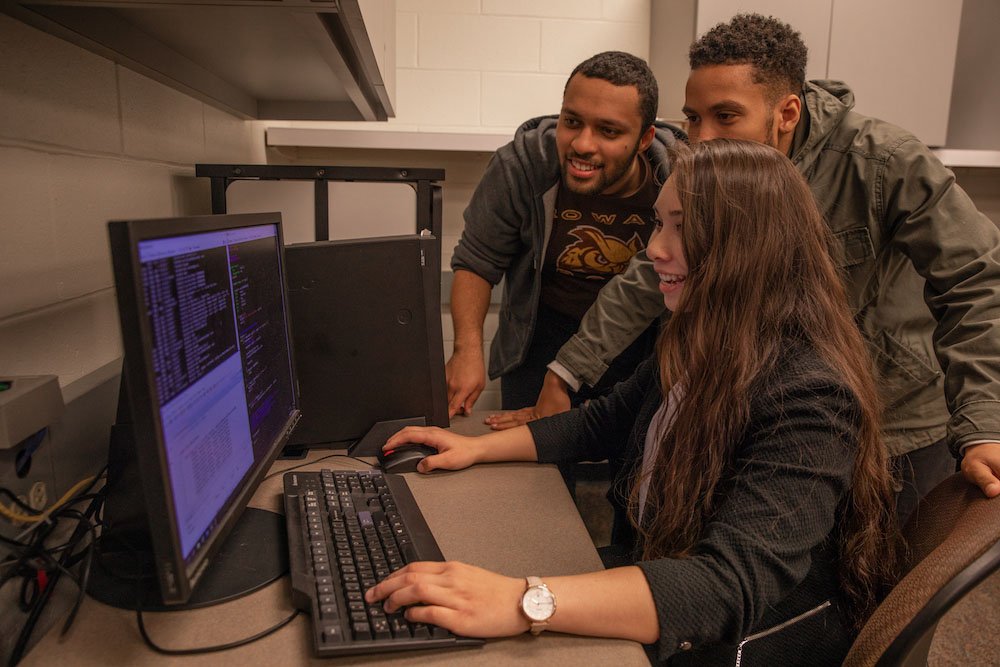 Three students are looking at a desktop computer screen