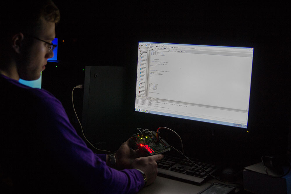 A computing and informatics major at Rowan University in dark room looks at a computer screen.