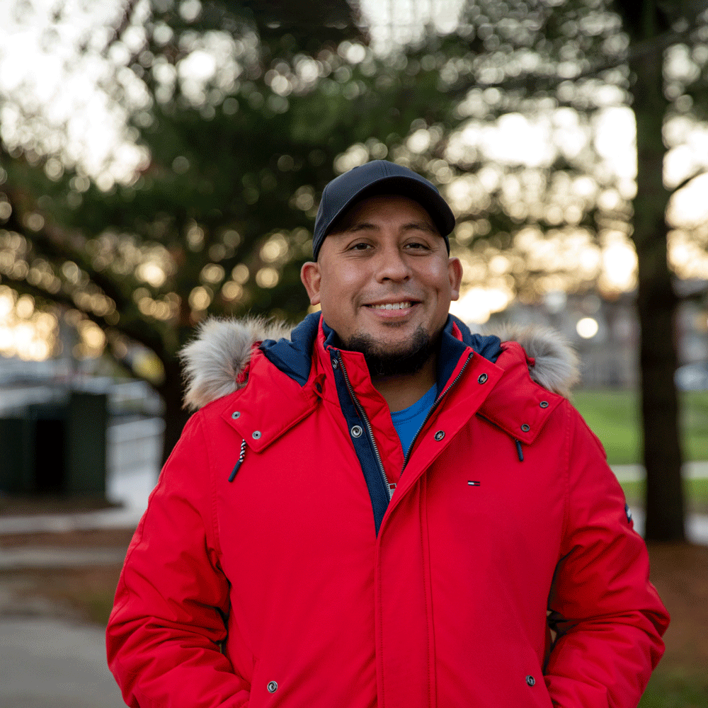 Michael wears a red coat outdoors on campus.