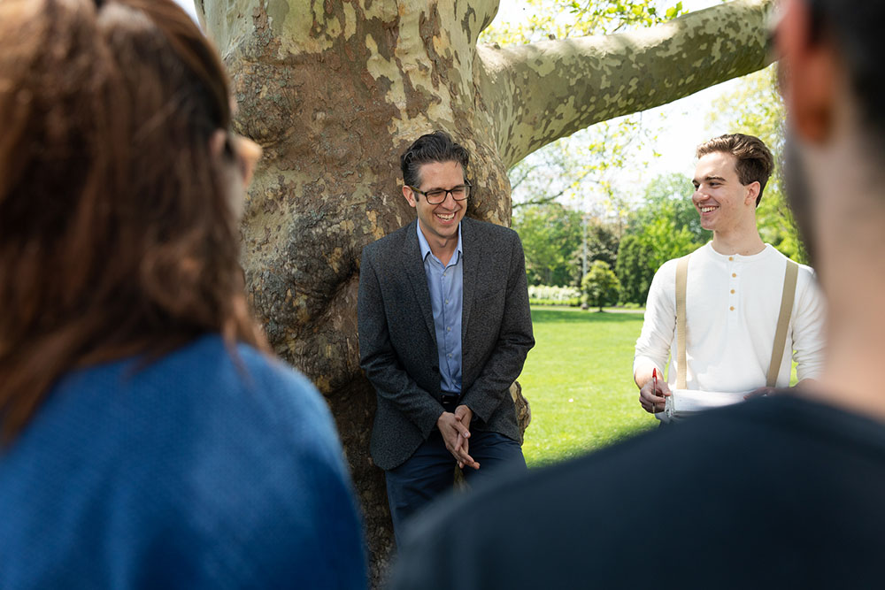 Faculty and students talking under a large, established tree