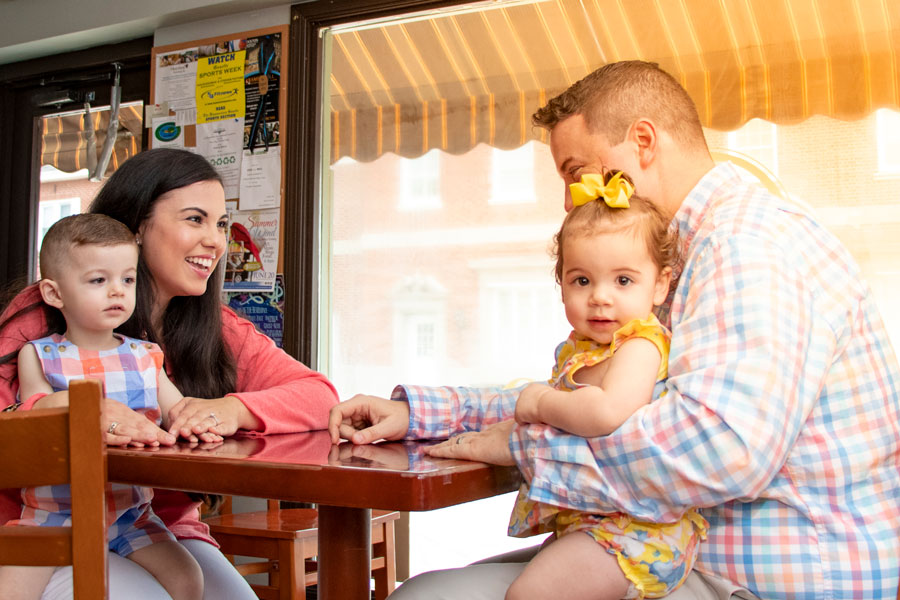 Christina sits at a table with her husband with her baby on her lap