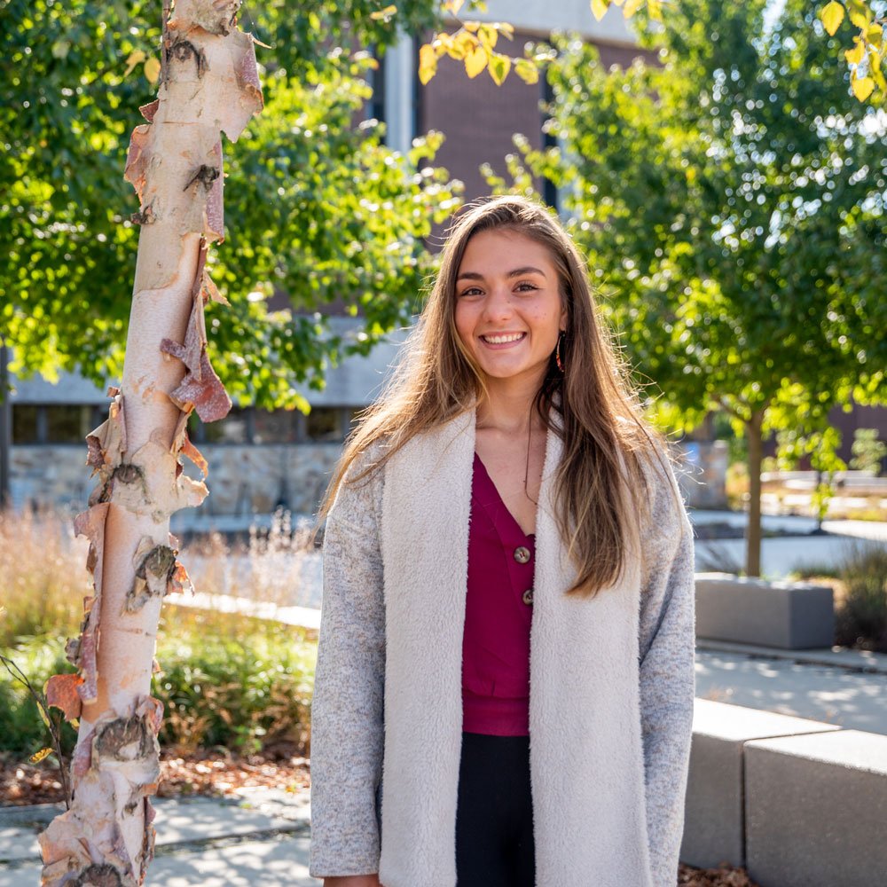 Gabriela stands next to trees outside on campus.