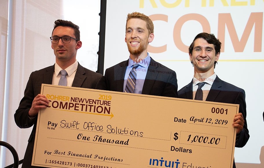 Business students standing on stage with a large check.