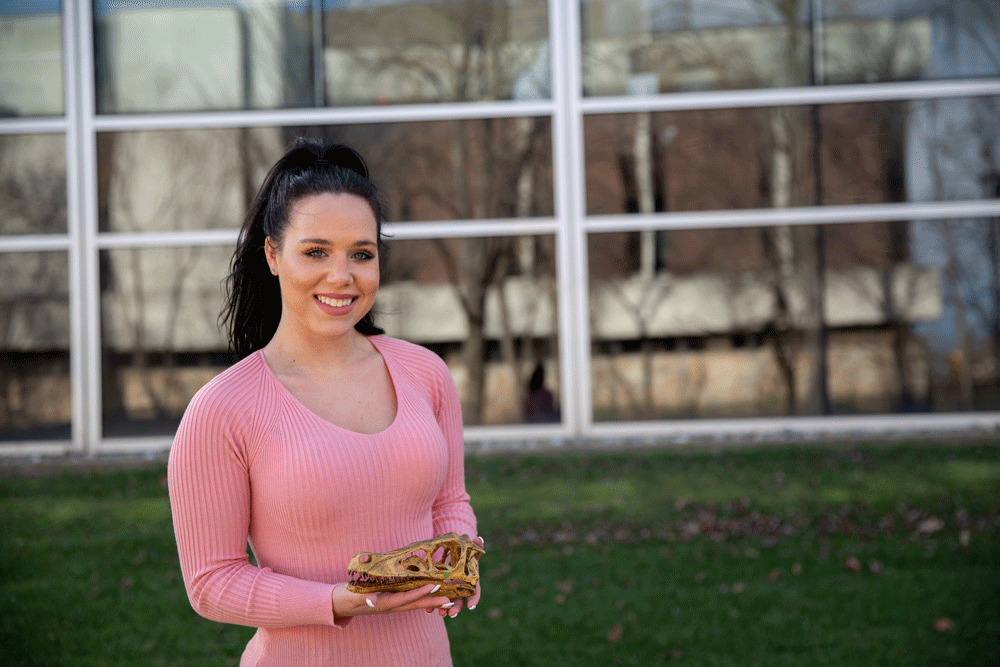 Kayla B. holds a fossil outside an academic building.