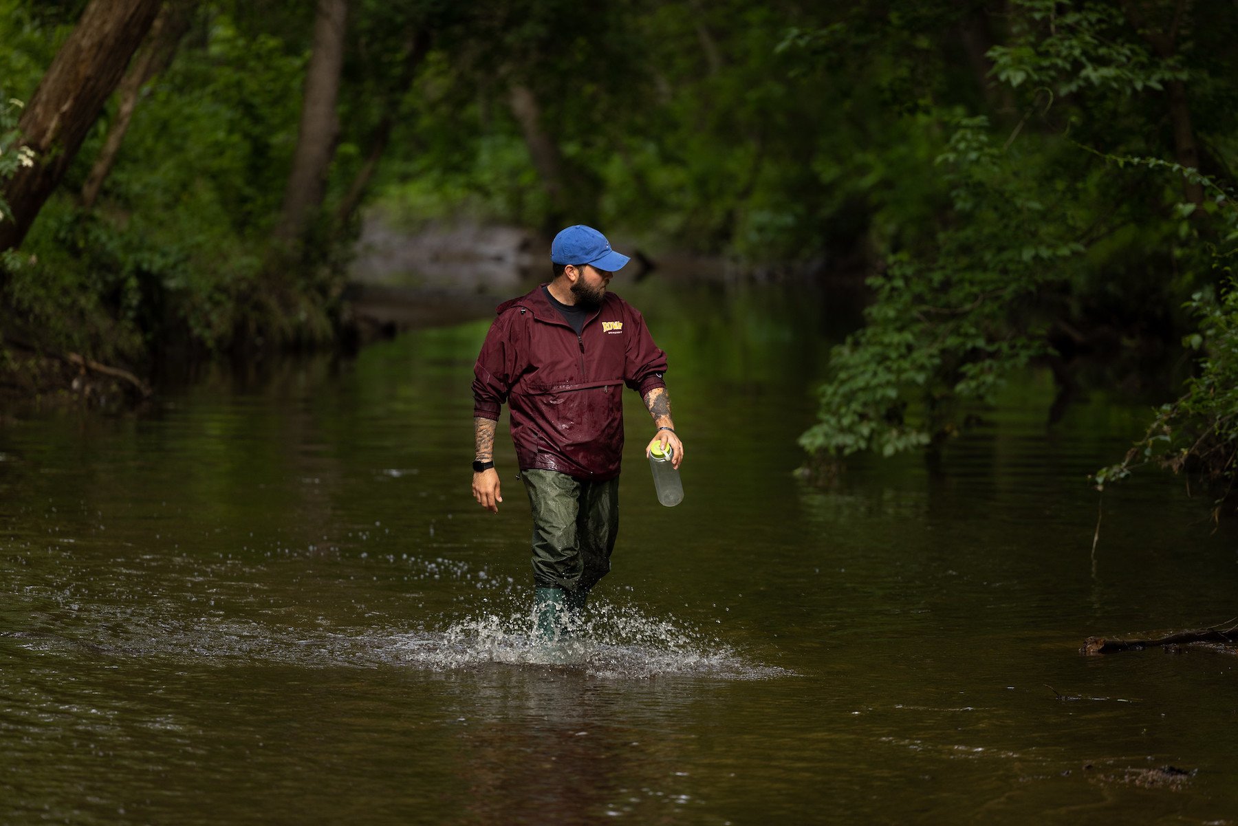 A student stands in a river with a water collection sample.
