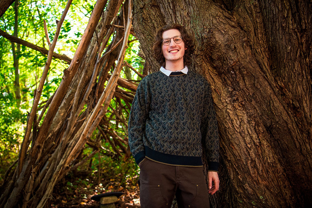 Brandon leans against a tree on campus.