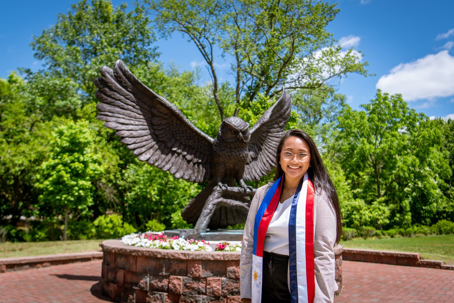 A student standing in front of the owl statue with a french banner.
