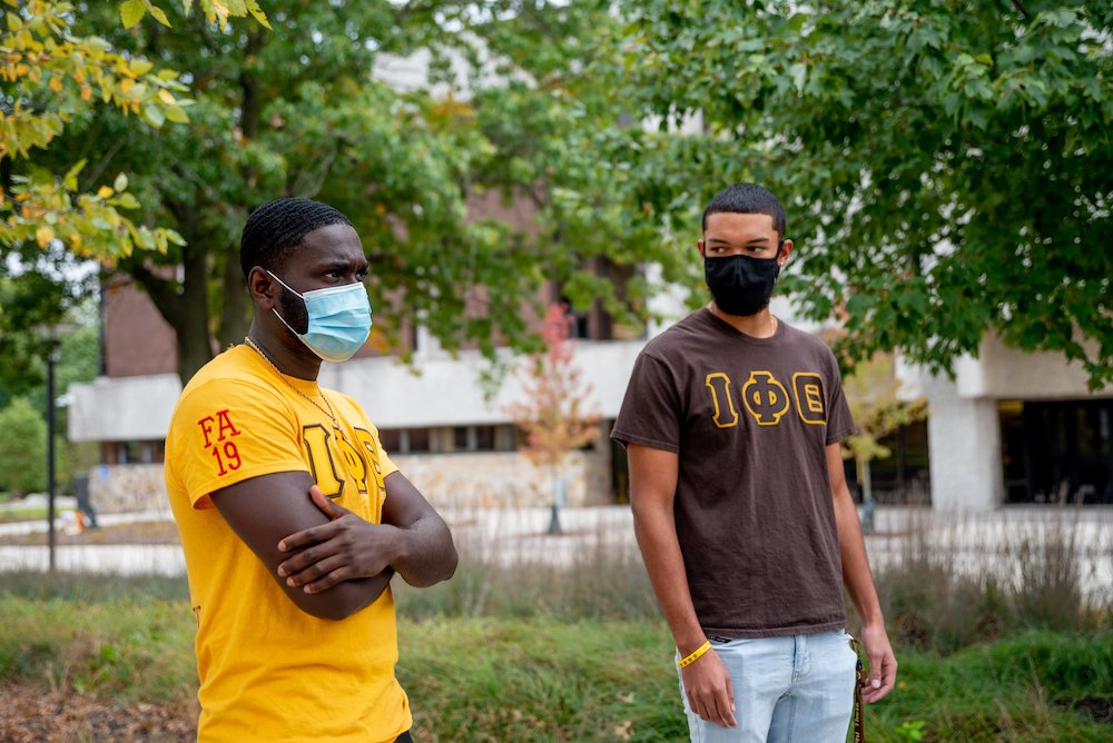 Two male students wearing Greek letters wearing masks on campus.