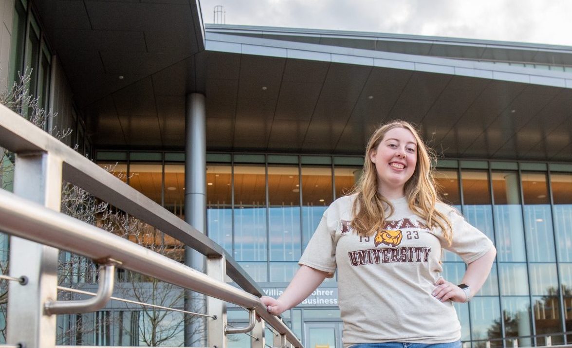 Rowan University student Paige stands behind Business Hall wearing a Rowan shirt. 