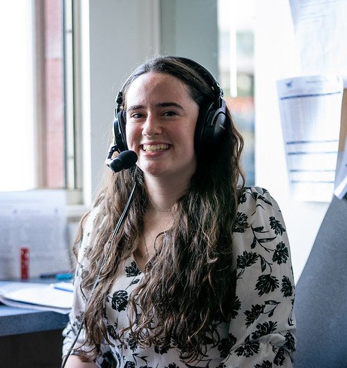 Rowan University radio student sits smiling while wearing a headshot on her head. 