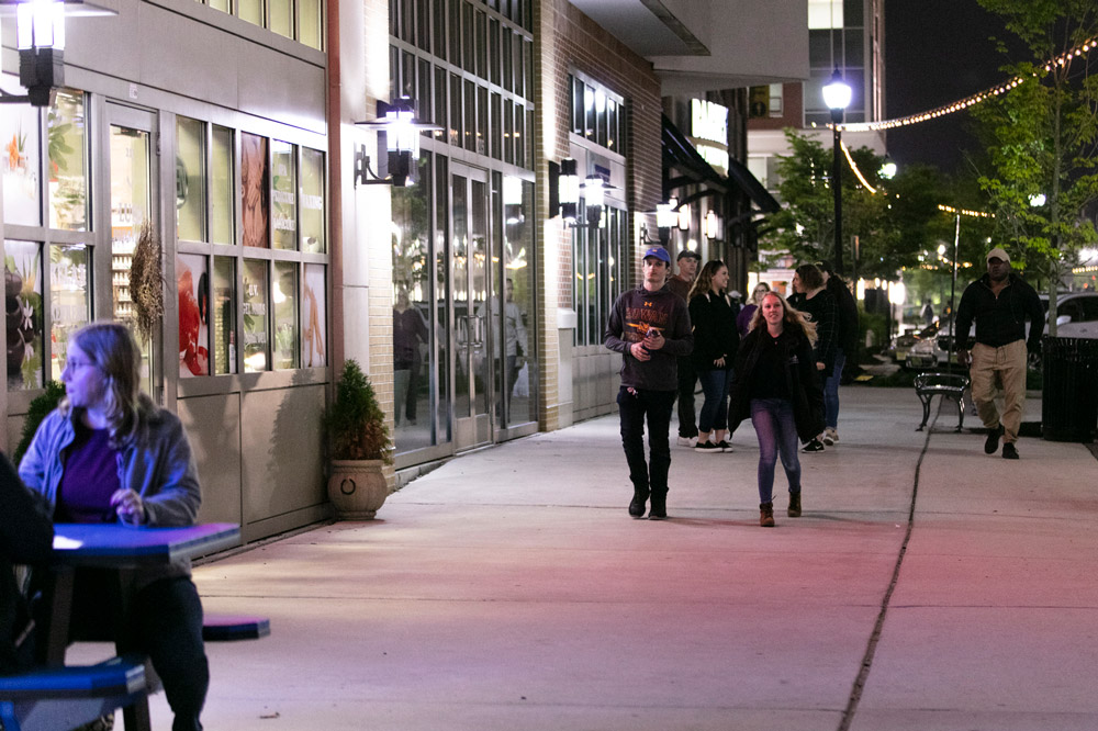 students laugh walking down Rowan Boulevard together at night with lights twinkling behind them