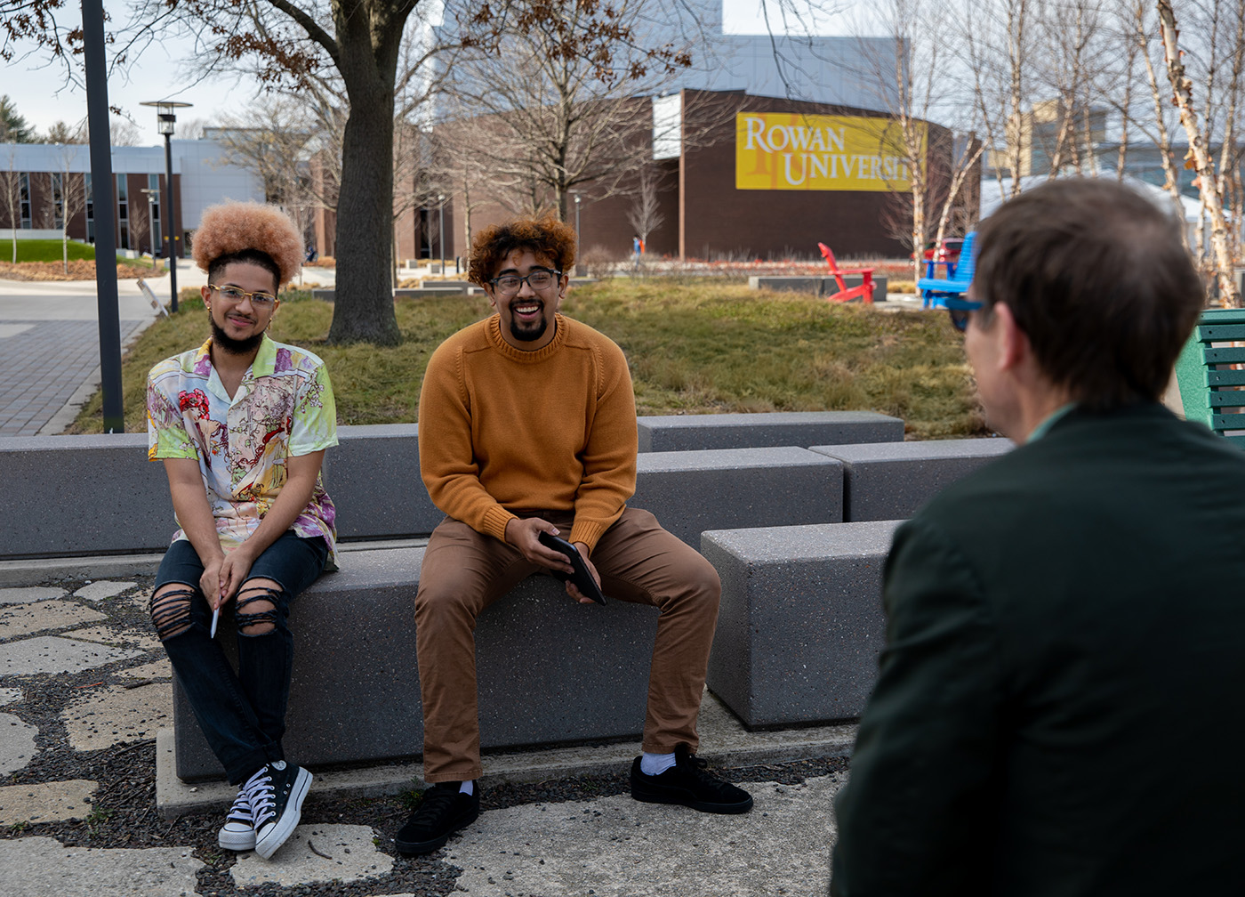 Two male students sitting on stone benches laughing.